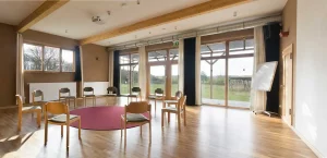 Seminarraum Strohtel: großer heller Raum mit einem Stuhlkreis und einem Teppich in der Mitte. Am Rand steht ein Flipchart, im Hintergrund eine große Fensterfront mit Blick ins Grüne.